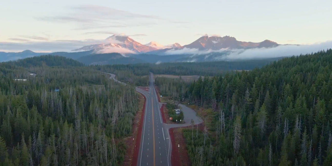 Scenic highway winding through Oregon's Cascade Mountains with snow-capped peaks in the distance
